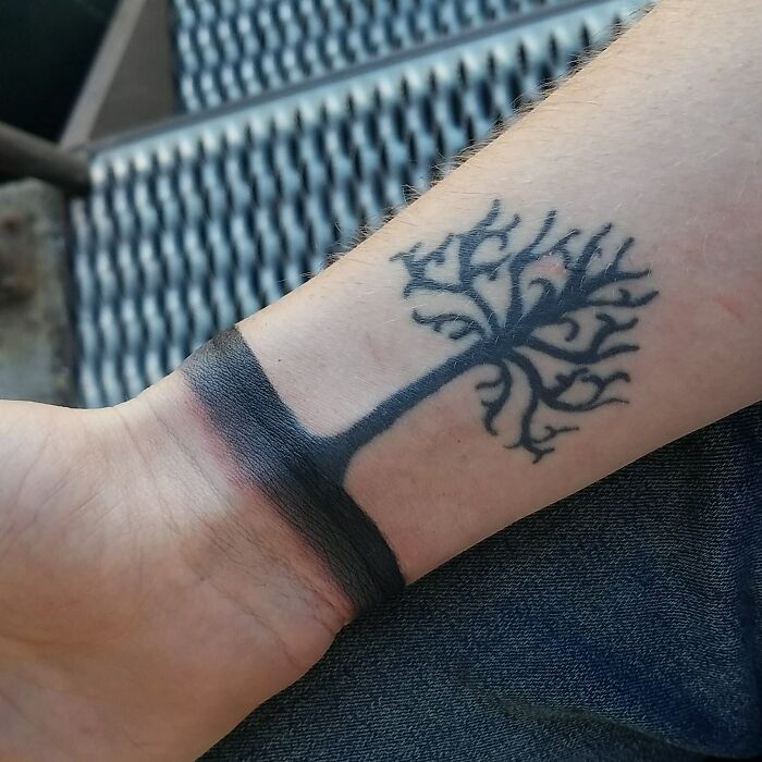 Tree wrist tattoo with detailed branches and a solid black band around the wrist.
