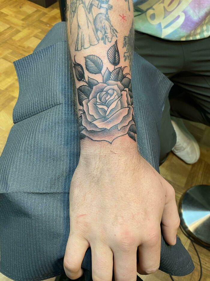 Wrist tattoo featuring a detailed black and gray rose design on the forearm.