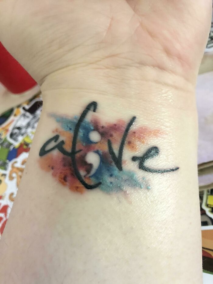 Wrist tattoo with the word "alive" in a cursive font and watercolor background.