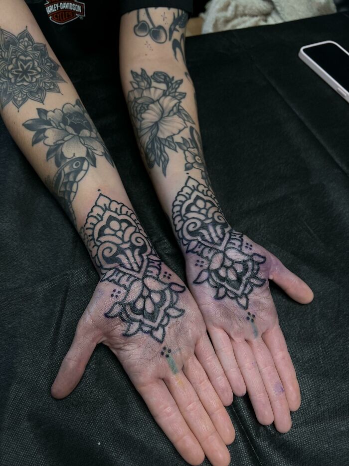 Ornate wrist tattoos on both hands featuring floral and geometric designs.