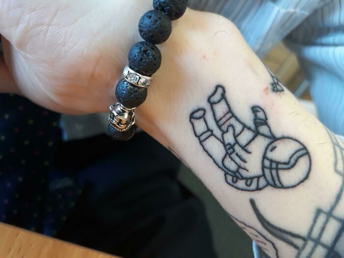 Astronaut wrist tattoo design next to a black beaded bracelet.