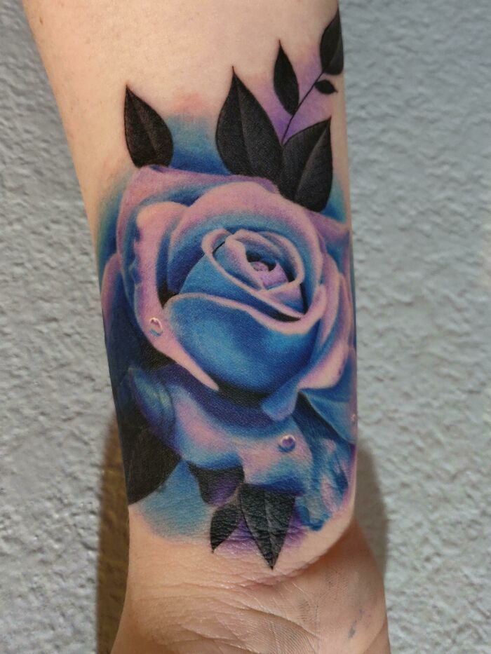 Blue rose wrist tattoo with black leaves, showcasing bold and modern design ideas.