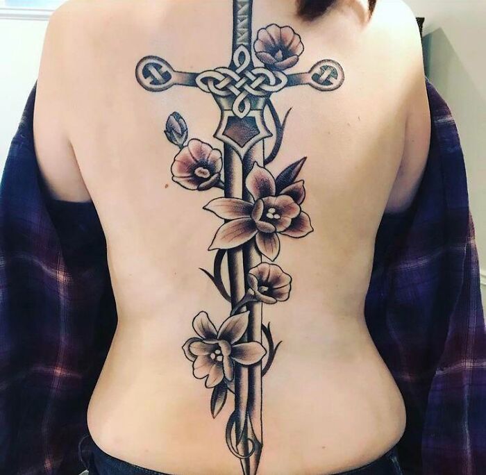 Intricate spine tattoo featuring a sword intertwined with flowers and Celtic designs.