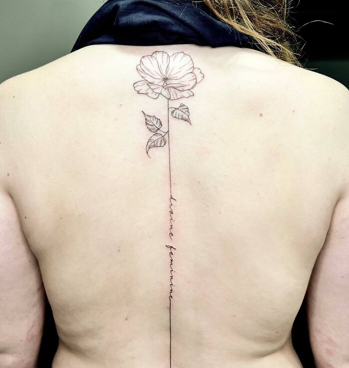 Elegant spine tattoo featuring a single line floral design with the text "divine feminine."