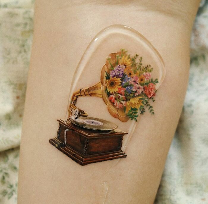 Color tattoo of a vintage gramophone with flowers, showcasing museum-quality artistry by Saegeem.