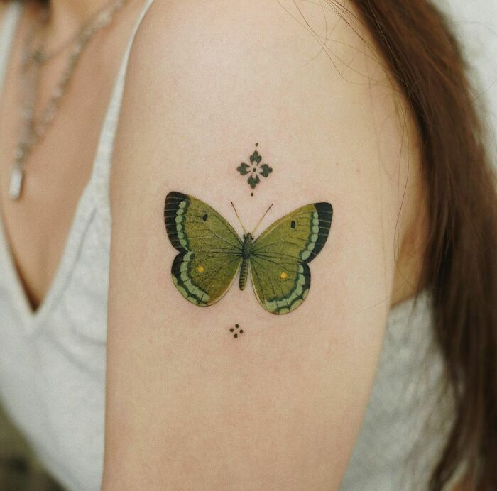 A vibrant butterfly color tattoo by Saegeem on an arm, adorned with additional delicate designs.