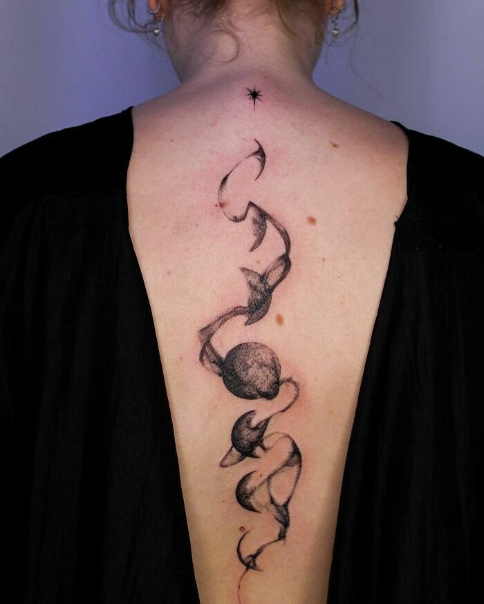 Elegant spine tattoo featuring abstract celestial design on a woman's back.