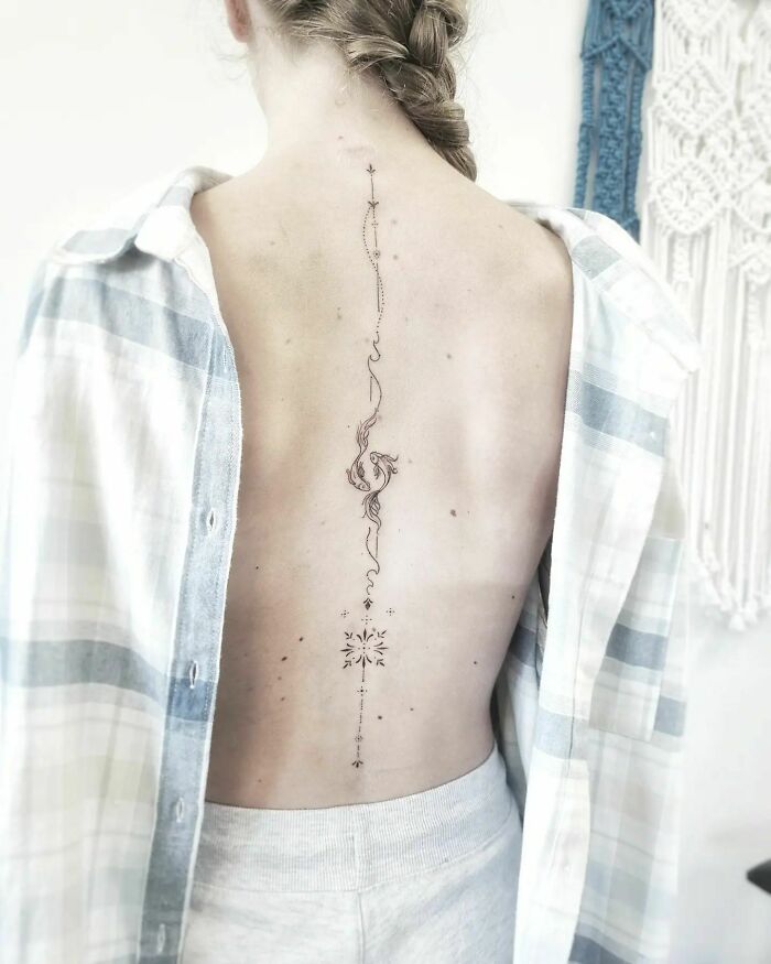 Elegant spine tattoo on woman's back, featuring delicate linework and artistic design.