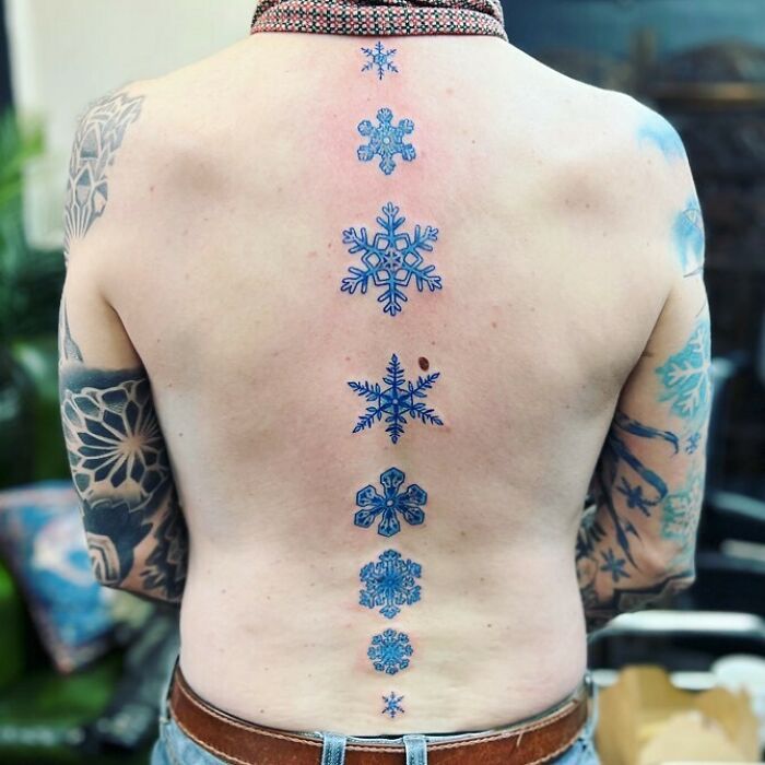 Blue snowflake spine tattoos on a person’s back, showcasing intricate and beautiful designs.