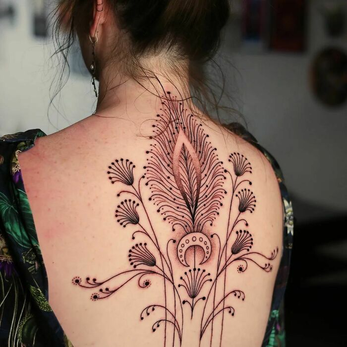 Elegant spine tattoo featuring intricate feather and floral design on a woman's back.