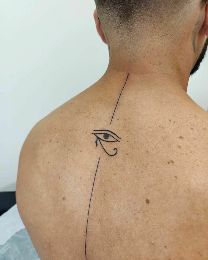 Minimalist spine tattoo featuring an Eye of Horus design.