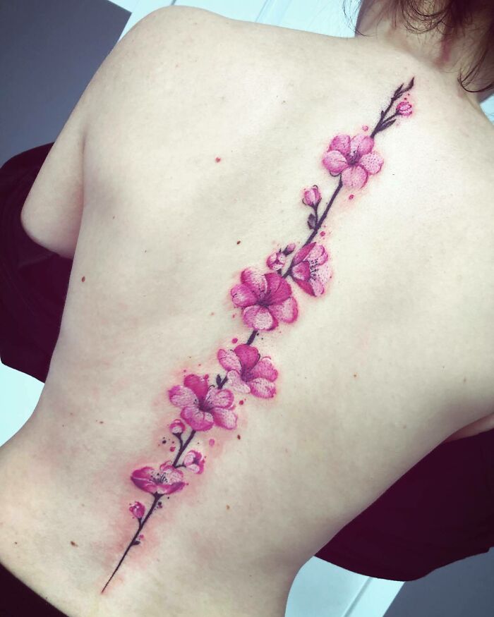 Elegant spine tattoo with pink flowers on a person's back, showcasing intricate and artistic design.