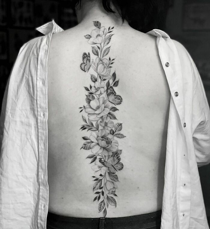 Elegant spine tattoo with floral and butterfly design on a person's back, showcasing intricate detail and symmetry.