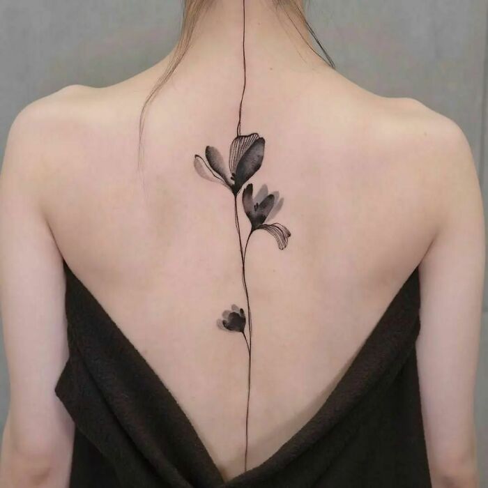 Elegant floral spine tattoo on woman's back, highlighting intricate ink artistry.