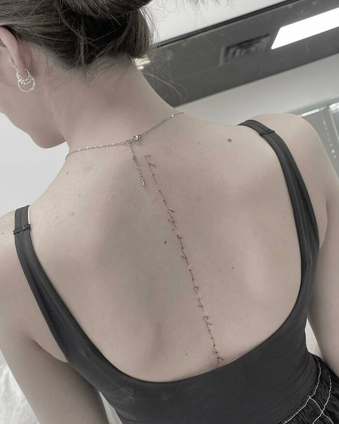 Elegant spine tattoo featuring a delicate script design on a woman's back.