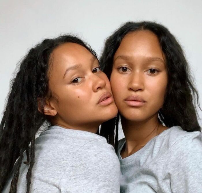 Portrait of celebrity twins with natural hair and gray shirts, showcasing beauty and bond in a simple studio setting.