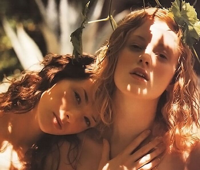 Two celebrity twins outdoors with soft natural light and leafy headpieces, showcasing their close bond and unique beauty.