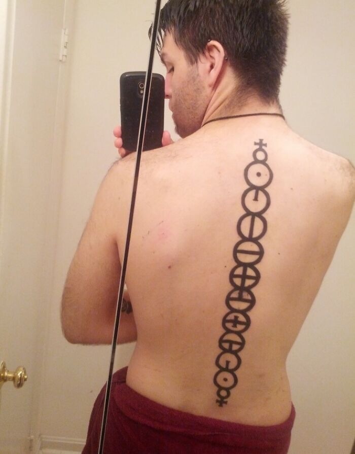 Man with an elegant spine tattoo featuring abstract circular designs, captured in a bathroom mirror selfie.