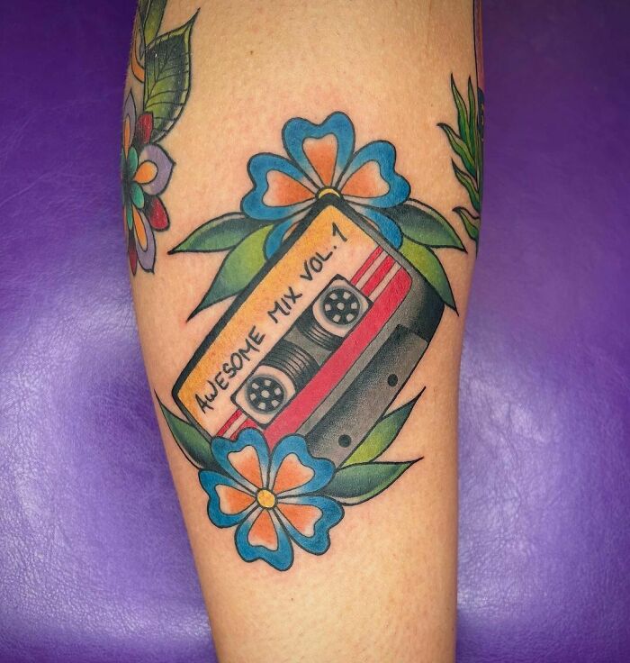 Marvel tattoo featuring "Awesome Mix Vol. 1" cassette with vibrant flowers, celebrating comic themes.