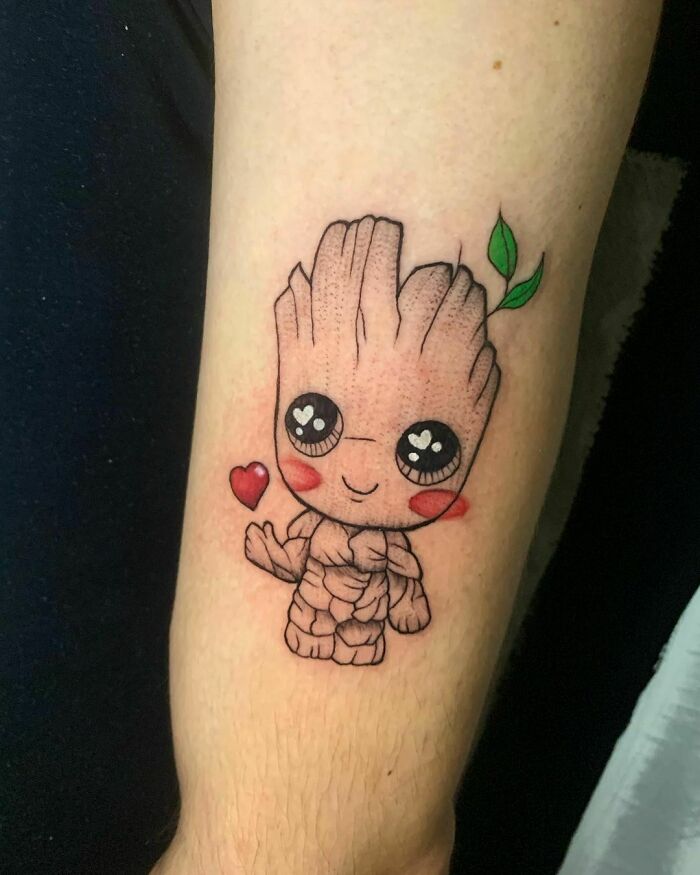 Cute Groot tattoo with heart detail, showcasing vibrant Marvel art on a forearm.
