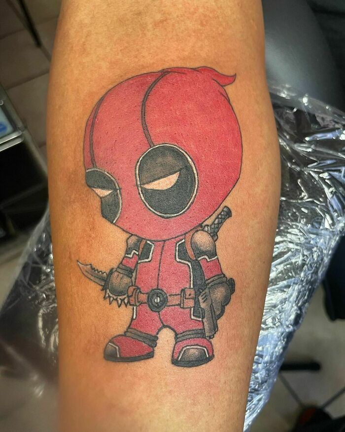 Marvel tattoo of a chibi-style character holding a small knife, inked on a person's arm.