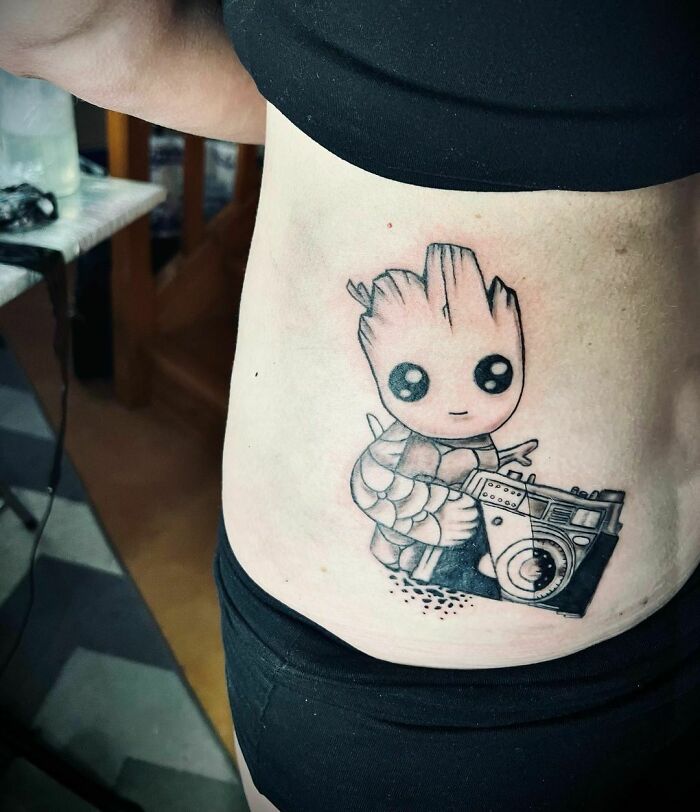 Marvel tattoo of a cute superhero character holding a cassette player on a person's side.