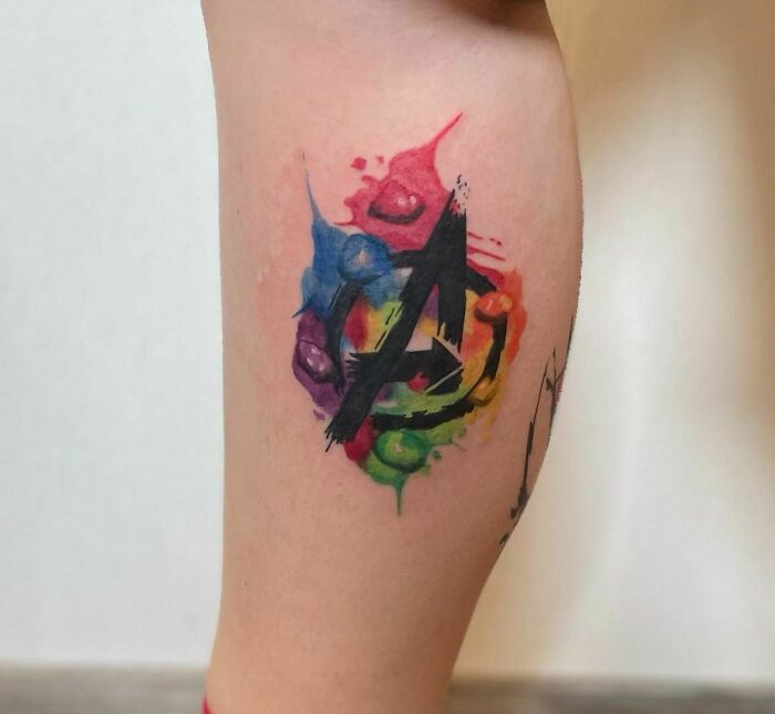 Colorful Marvel tattoo featuring the Avengers logo on a leg.