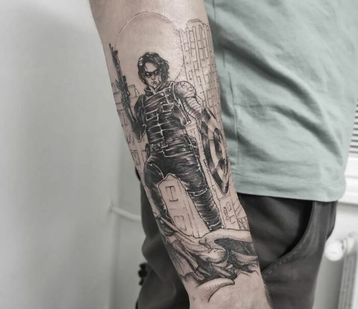 Marvel tattoo featuring a superhero character with a shield on an arm, showcasing intricate black and gray artwork.