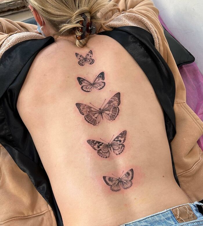 Elegant spine tattoo featuring a series of detailed butterfly designs down the back.
