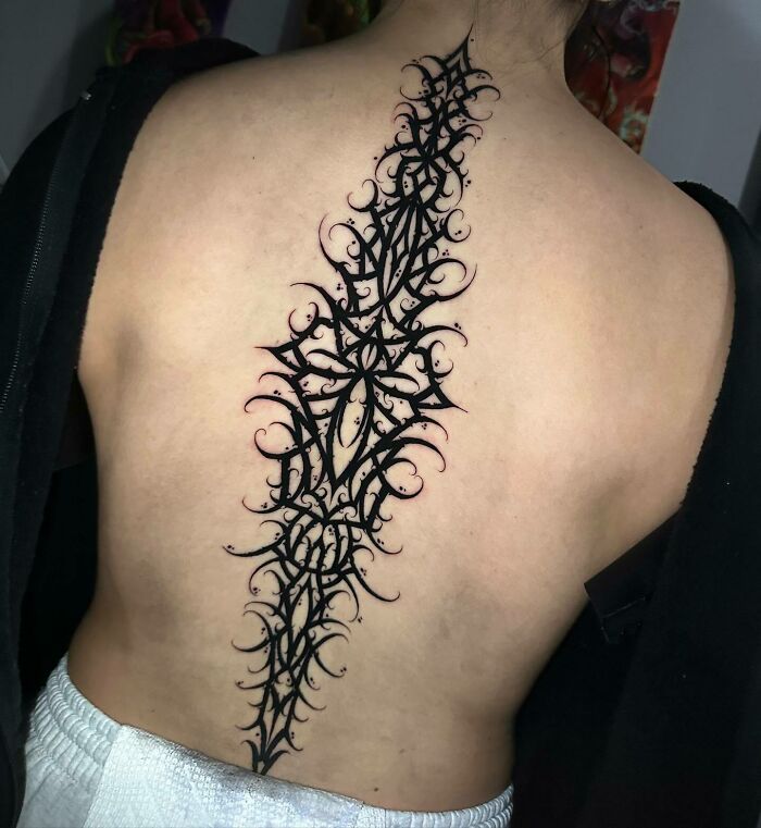 Intricate black spine tattoo design on a person's back, showcasing elegant tattoo art.
