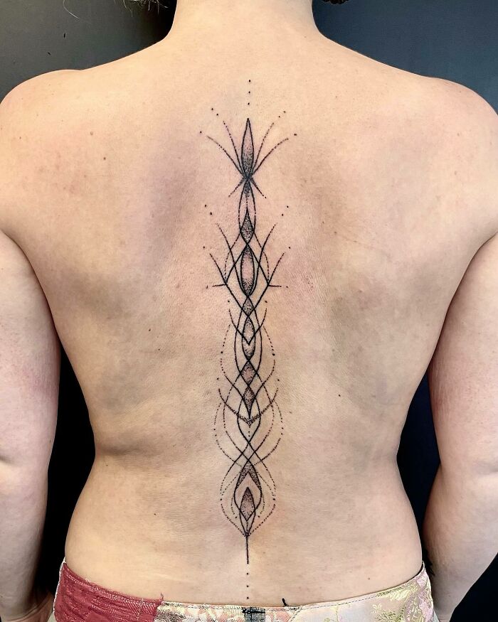 Elegant spine tattoo with intricate black line design on a person's back.