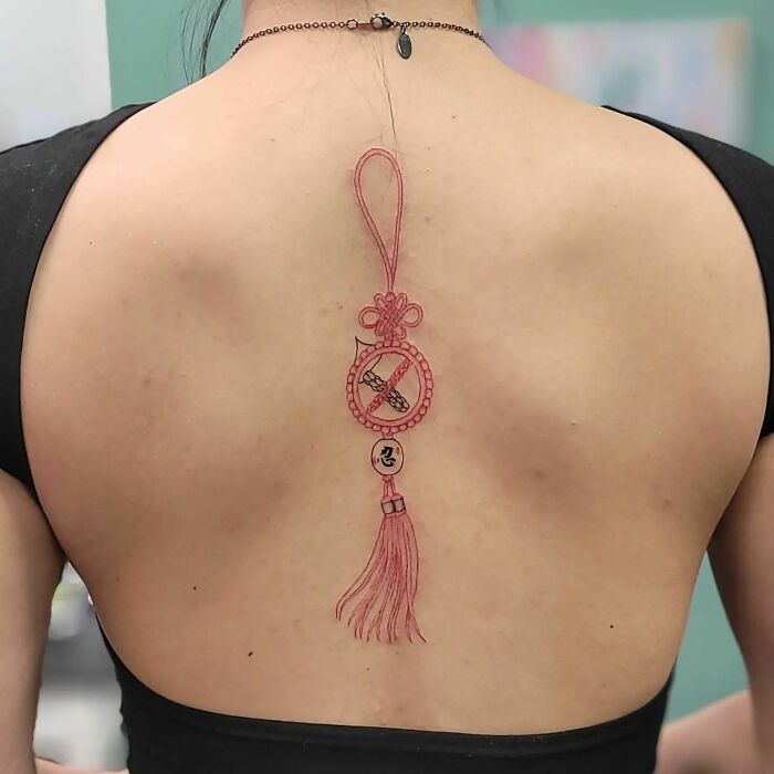 Beautiful spine tattoo featuring an intricate red design with tassel, symbolizing elegance and art.