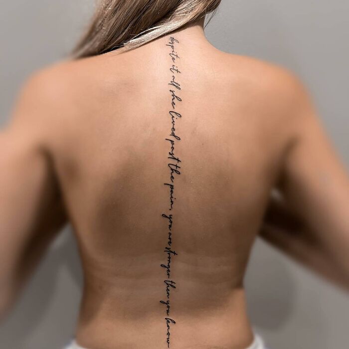 Elegant spine tattoo with cursive script on a woman's back, showcasing unique design ideas for body art.