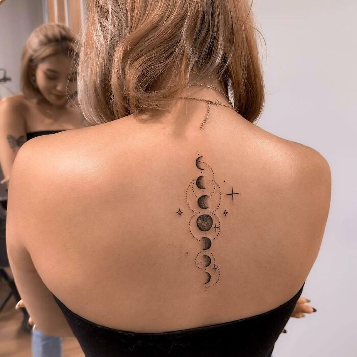 Woman with moon phase spine tattoo, featuring delicate dot and star details.