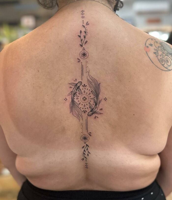 Elegant spine tattoo with floral and fish designs in a symmetrical pattern on a person's back.
