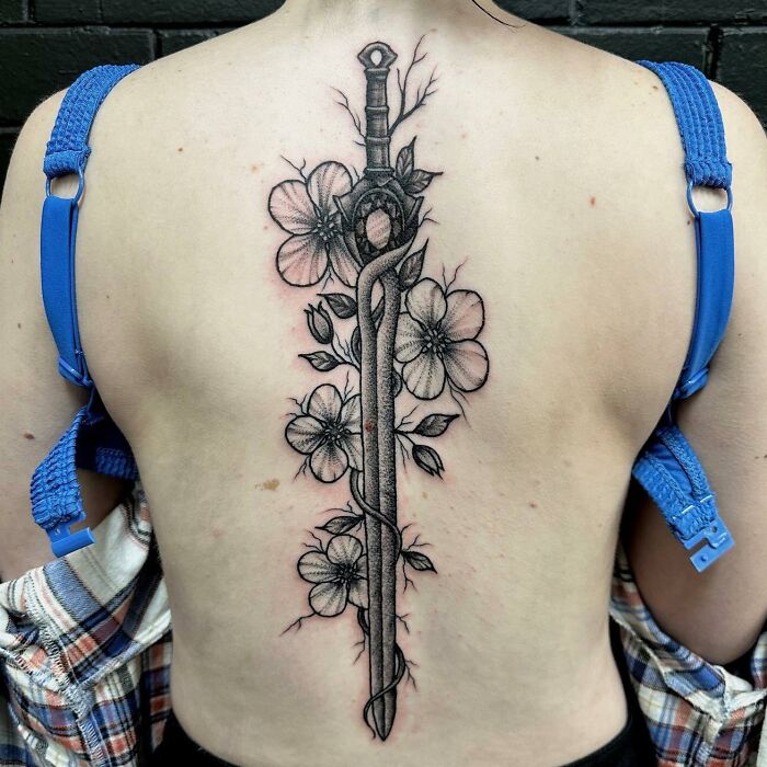 Floral and sword spine tattoo on back, intricate design and shading.