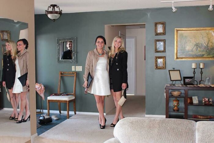 Two women posing for a picture in a room and man in a mirror reflection 