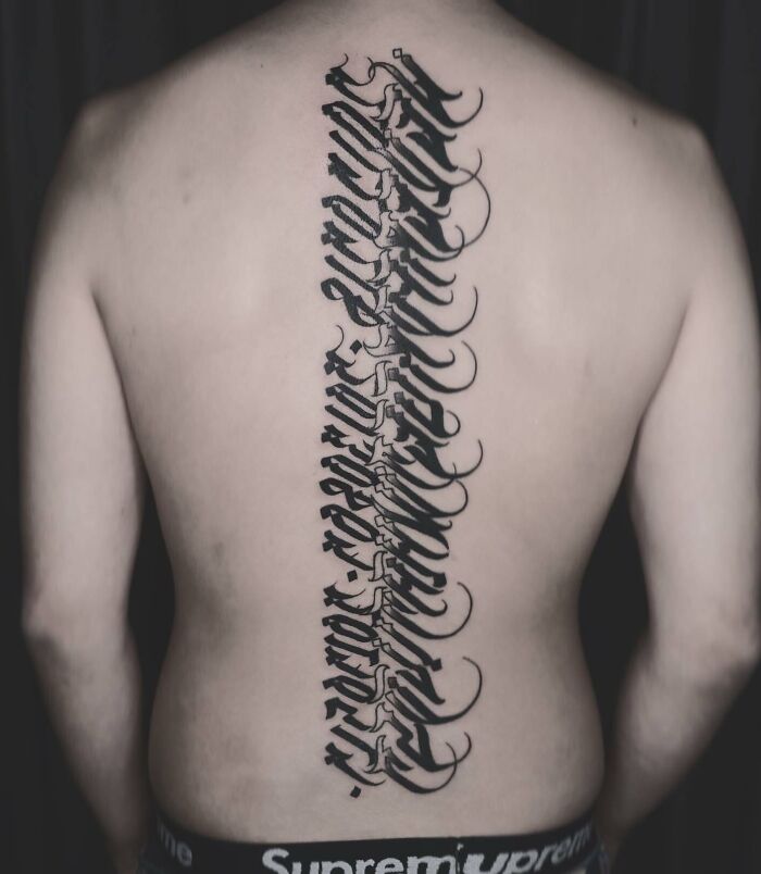 Elegant spine tattoo in bold script down the back, showcasing intricate design.