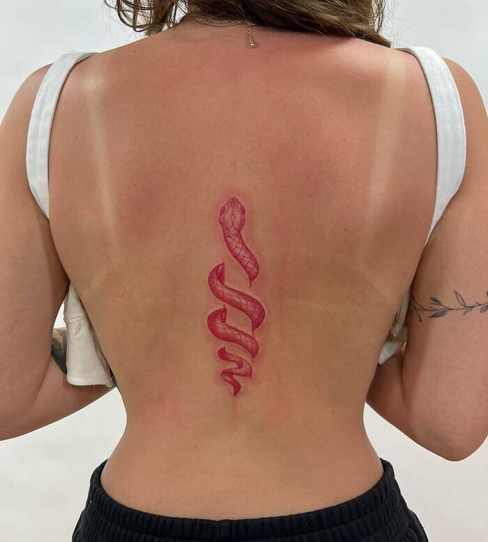 Elegant spine tattoo featuring a red snake design on a woman's back.