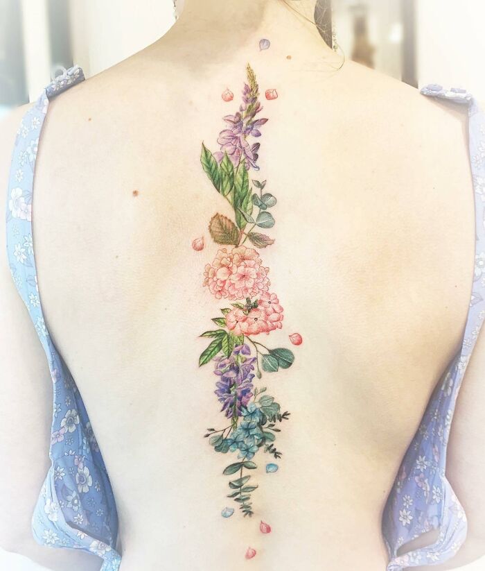 Elegant spine tattoo featuring colorful floral design on a woman's back.