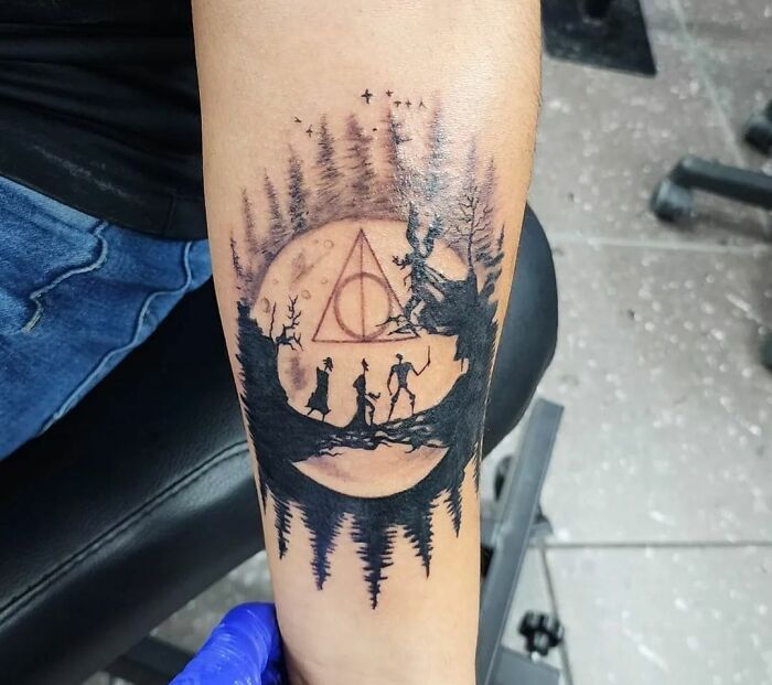 Harry Potter tattoo featuring silhouettes under a forest night scene, with the Deathly Hallows symbol in the background.