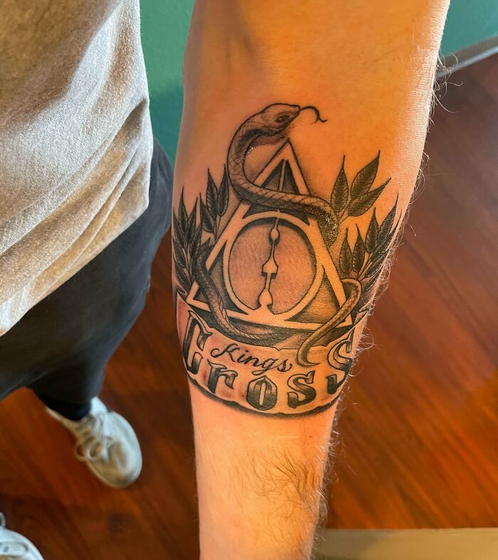 Arm tattoo featuring Harry Potter symbols: Deathly Hallows, snake, King's Cross text, and leaves.