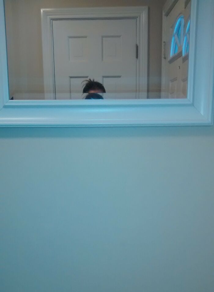 Small person taking a picture in front of a tall mirror 