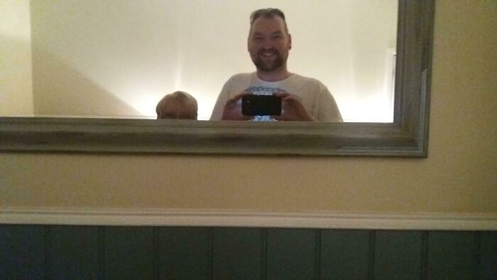 Tall man taking a mirror picture next to a small woman 