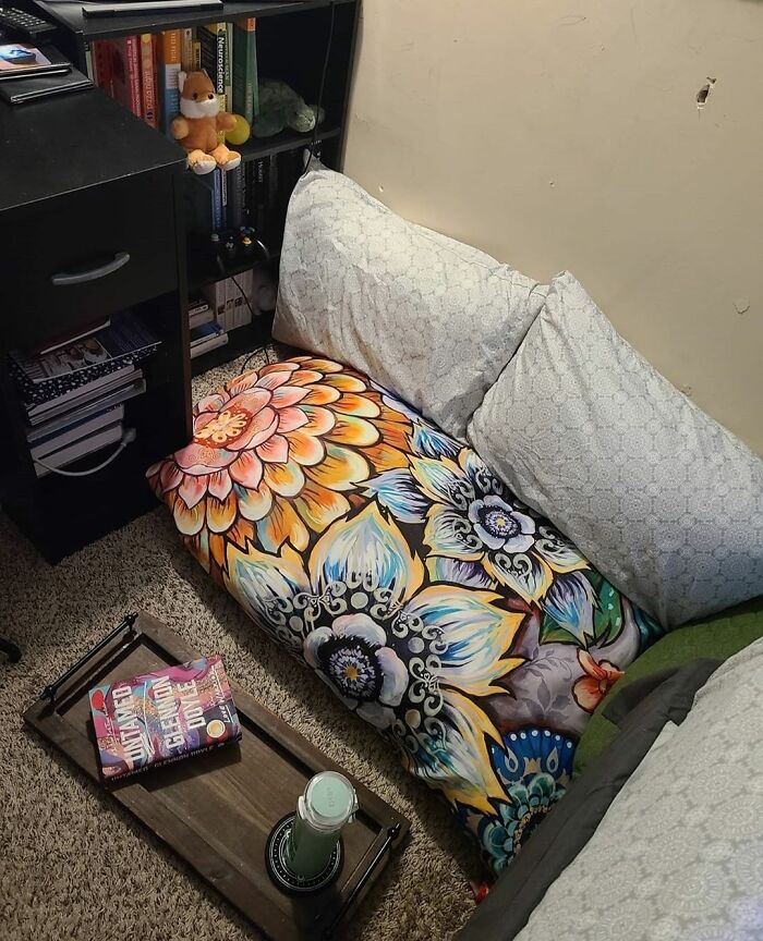 Cozy home decoration with floral cushions, a book, and a tea tray on a carpeted floor.
