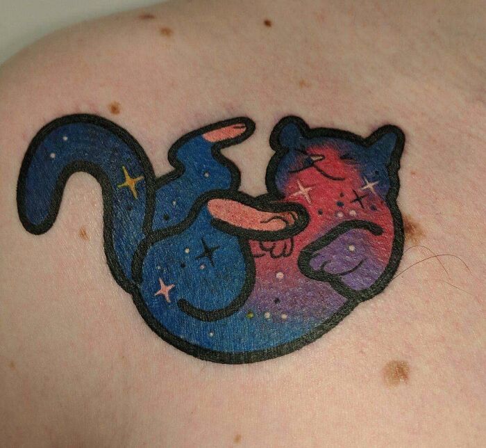 Space tattoo of a curled-up cat in a galaxy theme on skin, featuring stars and cosmic colors.