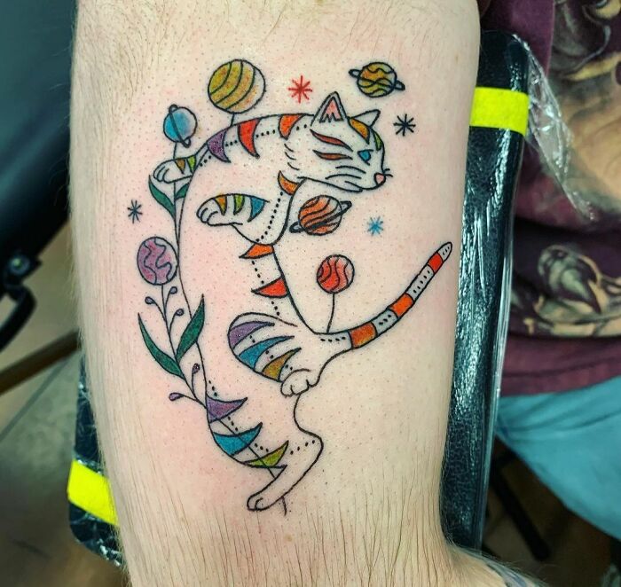 Colorful space-themed tattoo of a cat with planets and stars for astrology fans.
