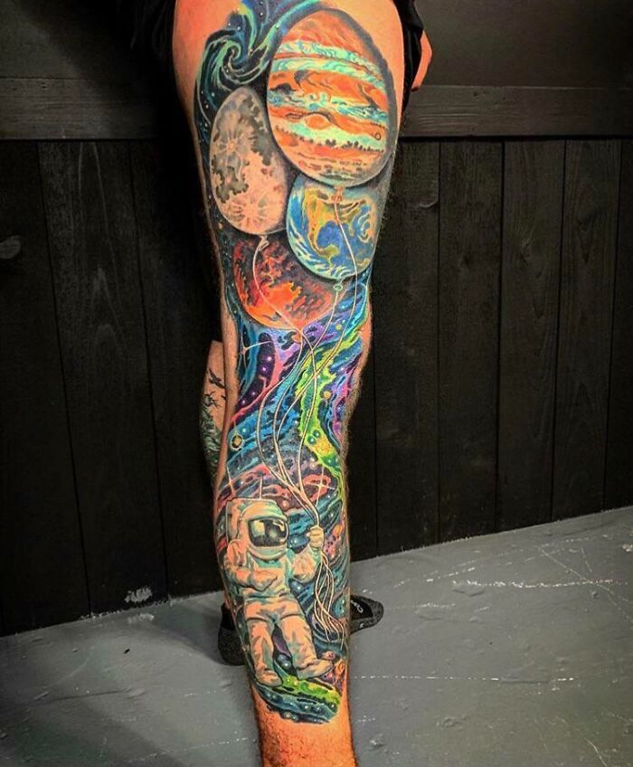 Astronaut and planets tattoo on a leg, showcasing vibrant space art for astrology enthusiasts.