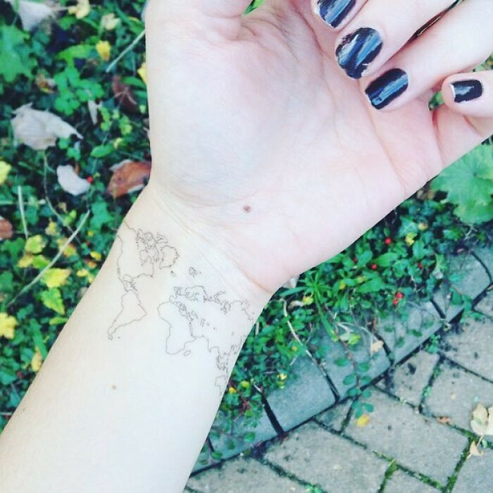 Wrist tattoo design featuring a small world map on a person's arm, surrounded by green foliage.