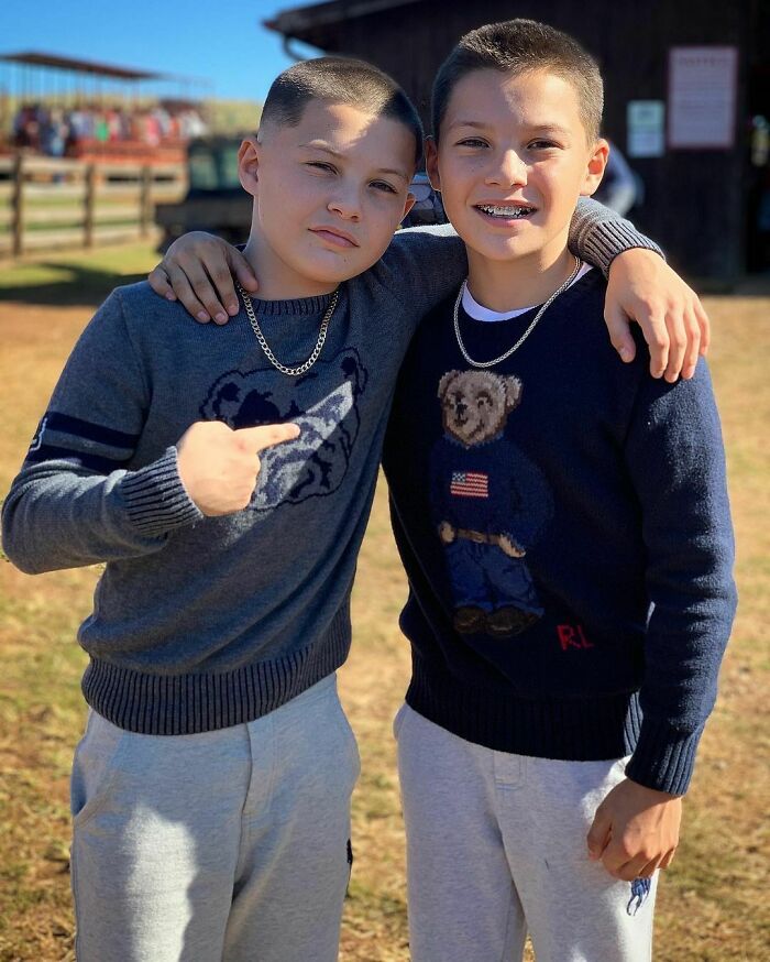 Two young twins wearing sweaters and chains pose outdoors showing close bond in celebrity twins photo.